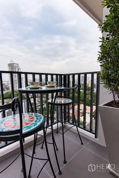 Condominium for sale in Watthana, Bangkok - Corner balcony with high bistro set and urban skyline outlook.