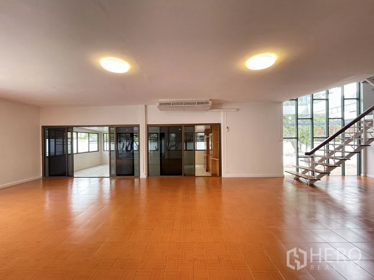 Home Office for rent in Din Daeng, Bangkok - Wide open room facing floor‑to‑ceiling glazing and a steel staircase with multiple sliding doors.