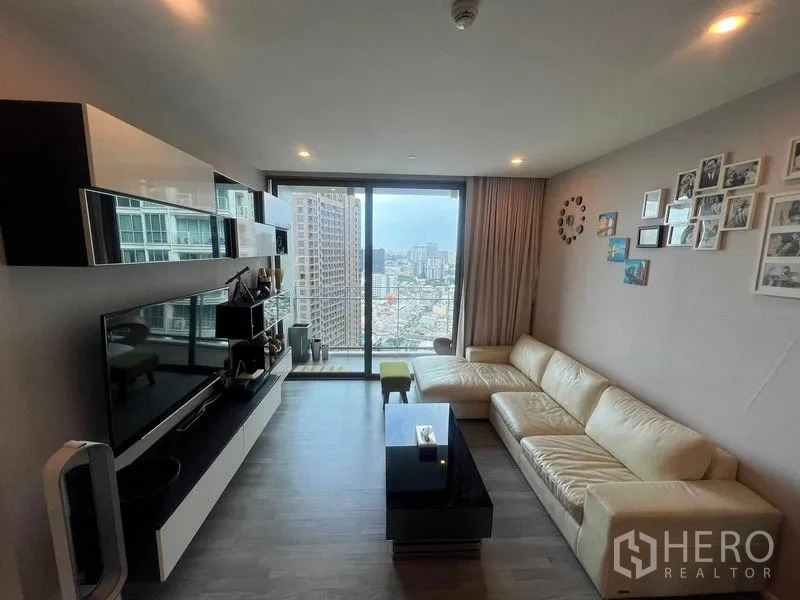 Condominium for rent in Khlong Toei, Bangkok - Contemporary living room with media wall and sliding glass doors to a city-view balcony.