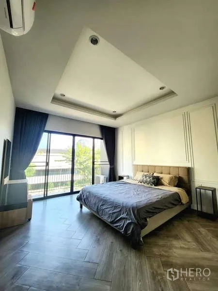 ทาวน์เฮาส์ ให้เช่าในWatthana, Bangkok - ห้องนอนมาสเตอร์เพดานหลุม เตียงคิงไซซ์ พื้นลายไม้ และประตูบานเลื่อนออกสู่ระเบียง