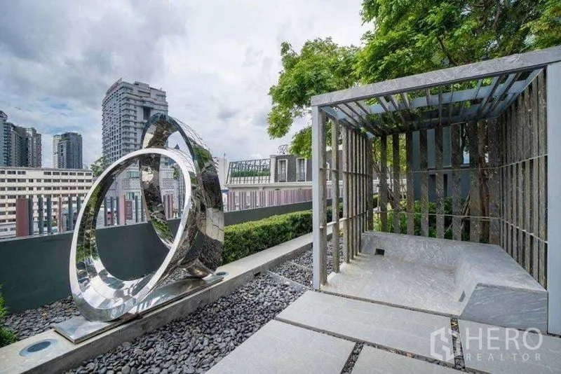 公寓 出租在Watthana, Bangkok - 屋顶露台带金属雕塑与遮蔽凉亭，眺望城市天际线。