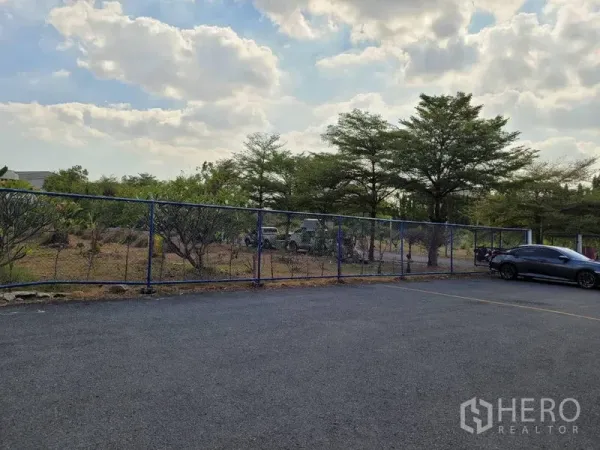 Warehouse for rent in Phra Khanong, Bangkok - Fenced outdoor parking area with asphalt surface and mature trees at a warehouse in Phra Khanong, Bangkok.