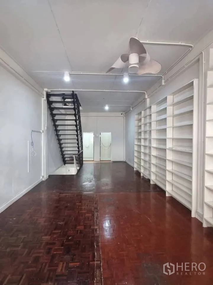 Shophouse for rent in Phra Khanong, Bangkok - Upper level with dark parquet floor, staircase, and wall-mounted shelving.