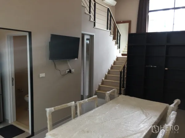 Townhouse for rent in Suan Luang, Bangkok - Open-plan living and dining space with staircase, shelving and a guest bathroom off the hall.