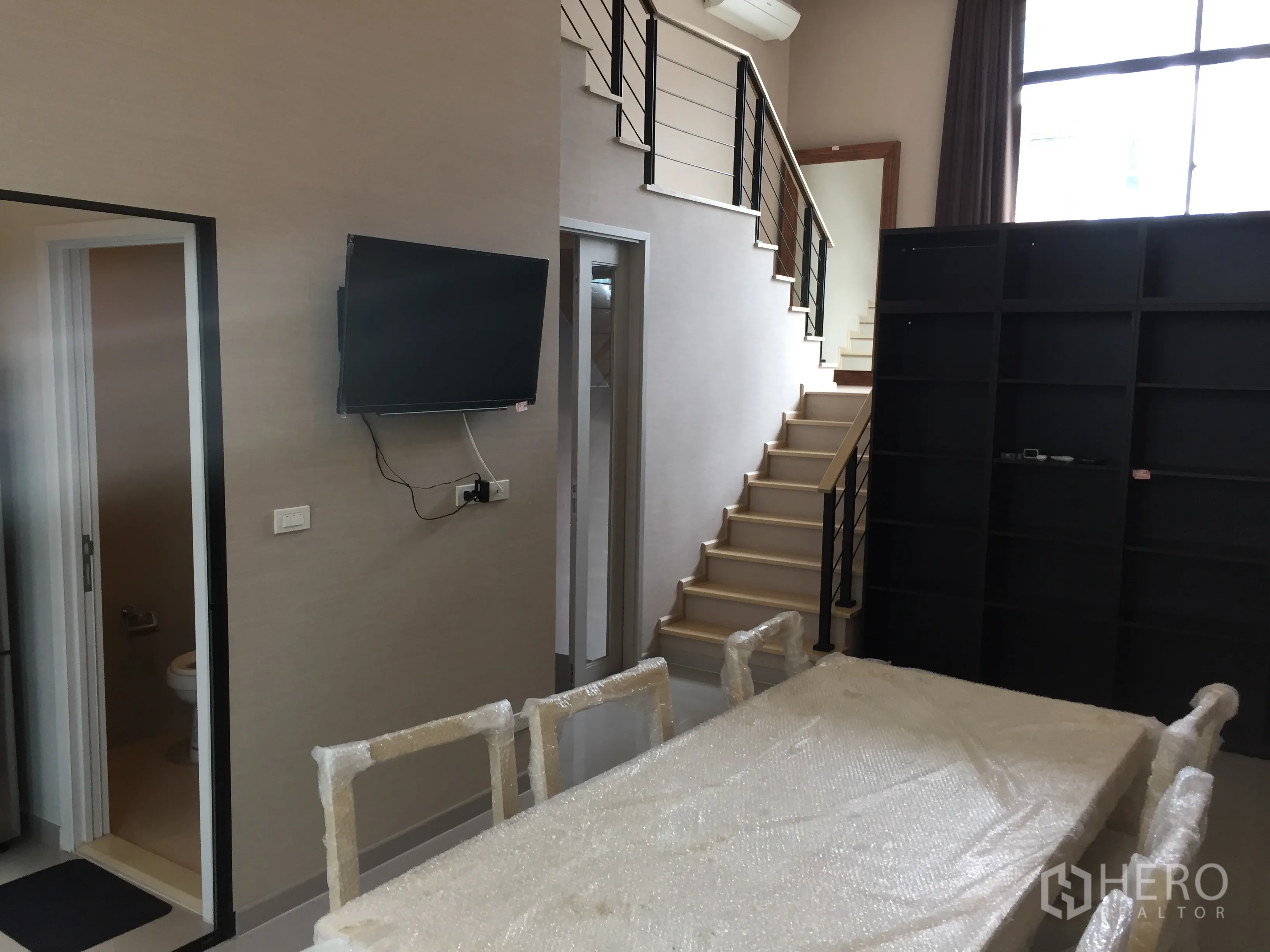 Townhouse for rent in Suan Luang, Bangkok - Open-plan living and dining space with staircase, shelving and a guest bathroom off the hall.