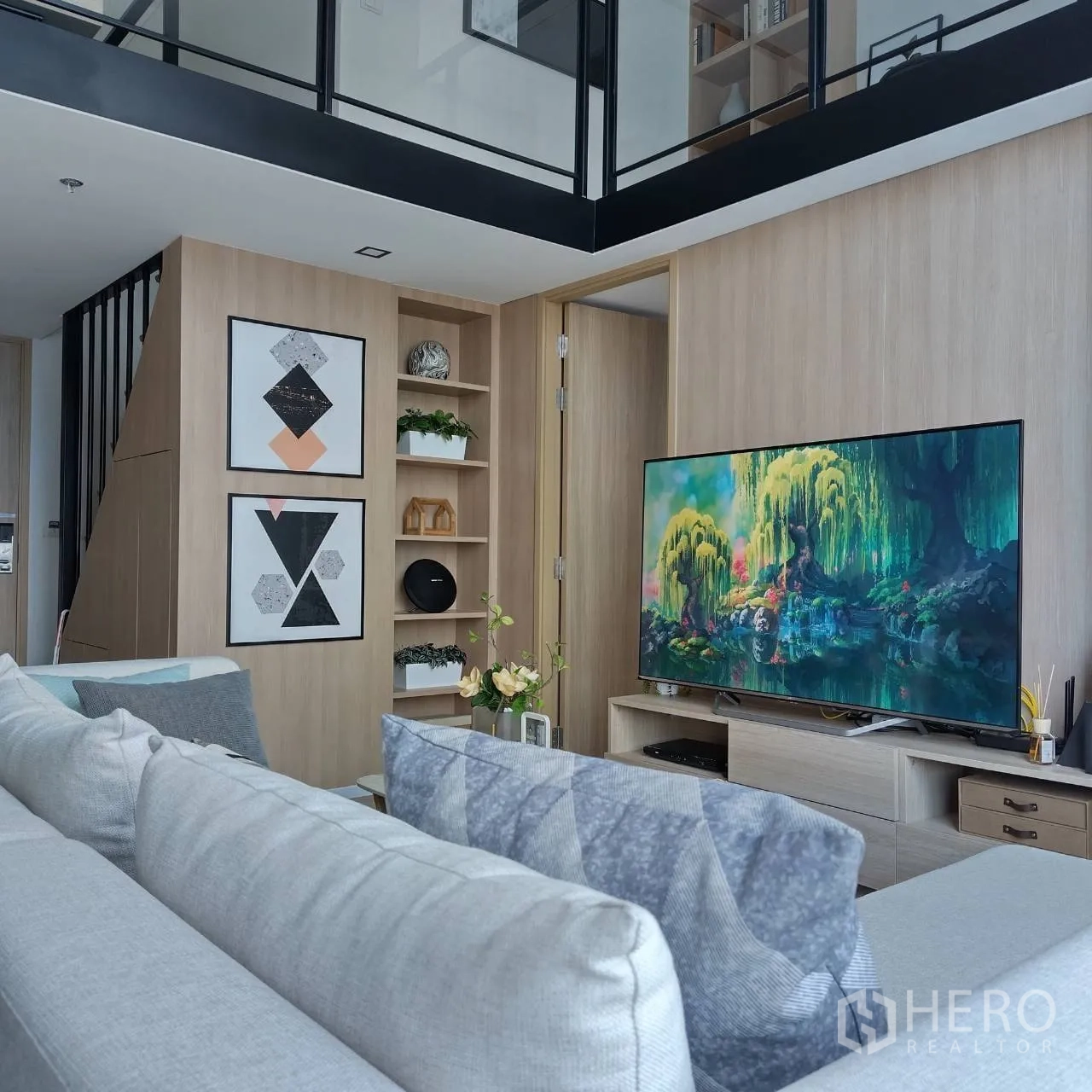 Condominium for rent or sale in Khlong Toei, Bangkok - Bright living room with sofa, TV console, wood accents, and mezzanine with black-framed glass.