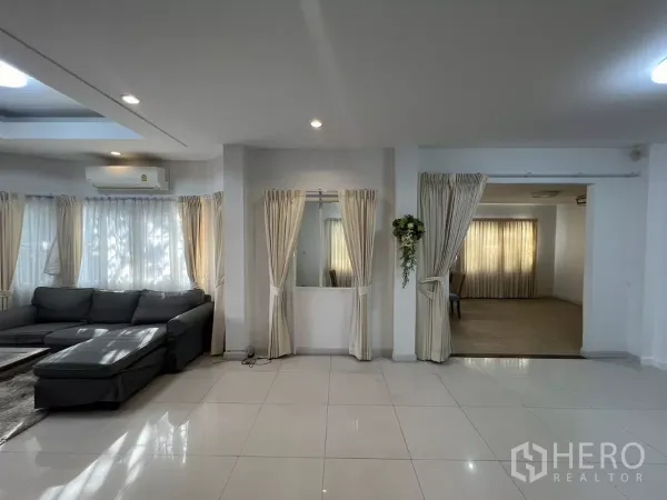 独立式住宅 出租在Bang Kapi, Bangkok - 客厅配转角沙发与纱帘，旁边为多功能房入口。