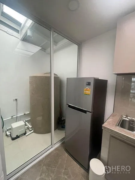 Townhouse for rent in Suan Luang, Bangkok - Kitchen and utility area with refrigerator beside a glass partition and outdoor water tank.