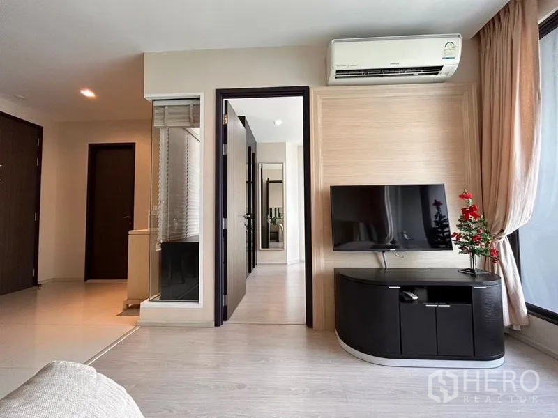 Condominium for rent or sale in Khlong Toei, Bangkok - Cozy living area with wall-mounted TV, air conditioning and doorway to the bedroom.