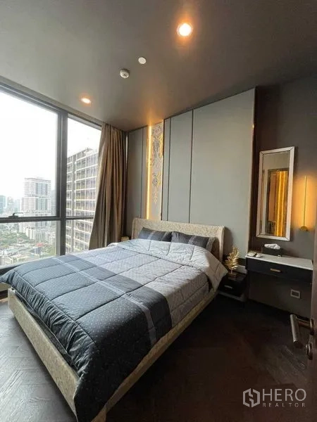 Condominium for rent in Khlong Toei, Bangkok - Bedroom with corner floor‑to‑ceiling windows, soft accent lighting and expansive city view.