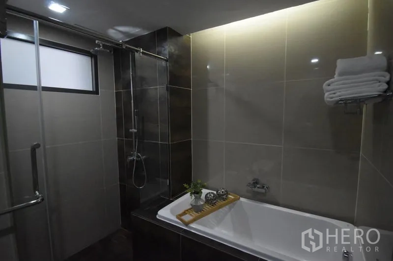 Condominium for rent in Khlong Toei, Bangkok - Contemporary bathroom featuring a separate glass shower and a bathtub with soft ambient lighting.