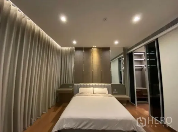 Condominium for rent in Khlong Toei, Bangkok - Cozy bedroom with feature headboard, bedside tables and sliding door to a walk-in closet.