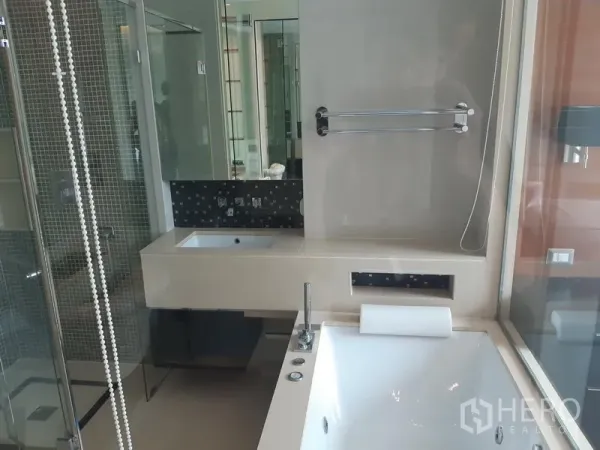 Condominium for rent in Khlong Toei, Bangkok - Contemporary bathroom with long vanity, soaking tub and glass-enclosed shower.