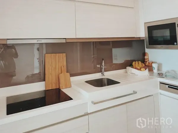Condominium for rent in Thon Buri, Bangkok - Sleek built-in kitchen with white countertops, induction hob and sink.