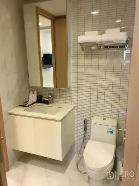 Condominium for rent in Watthana, Bangkok - Modern bathroom with tiled walls, vanity with mirror cabinet, toilet and towel rack.