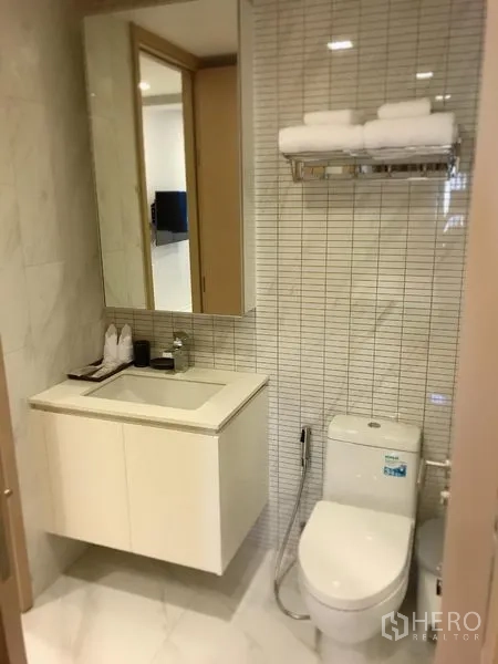 Condominium for rent in Watthana, Bangkok - Modern bathroom with tiled walls, vanity with mirror cabinet, toilet and towel rack.