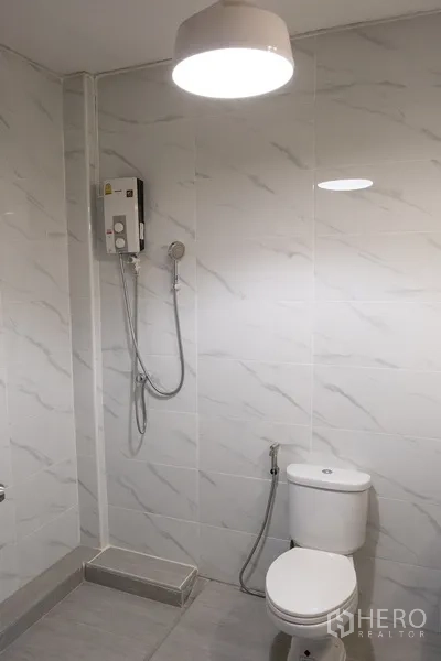 Home Office for rent in Khlong Toei, Bangkok - Modern bathroom with marble-look tiles, toilet and hot-water shower.