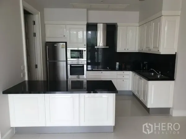 Condominium for rent in Watthana, Bangkok - Modern white U-shaped kitchen with black stone countertops, island, built-in oven and stainless refrigerator.
