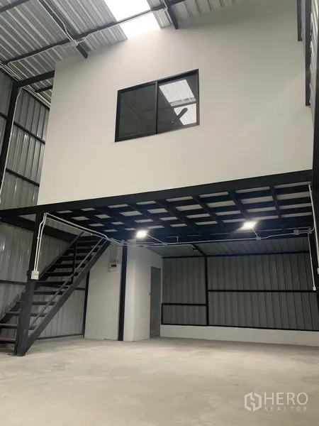 Warehouse for rent in Bangkok - Open warehouse floor featuring a steel mezzanine office, staircase, and bright LED lighting.