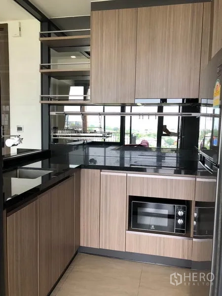 Condominium for rent in Watthana, Bangkok - Compact L‑shaped kitchen with black countertops, built‑in microwave, sink, and ample storage.