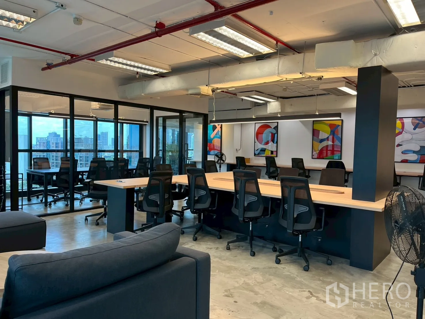 ออฟฟิศ for rent in Watthana, Bangkok - โซนออฟฟิศพร้อมโต๊ะหลายชุด โซฟา ผนังกระจก และภาพศิลป์สีสันสดใส