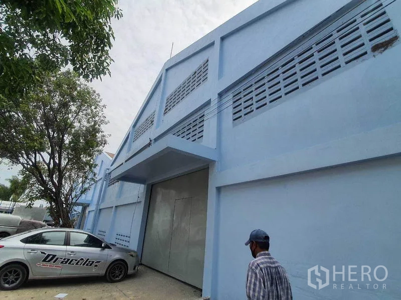 Warehouse for rent in Nakhon Pathom - Angled exterior of blue warehouse showing large metal sliding door and parking area.