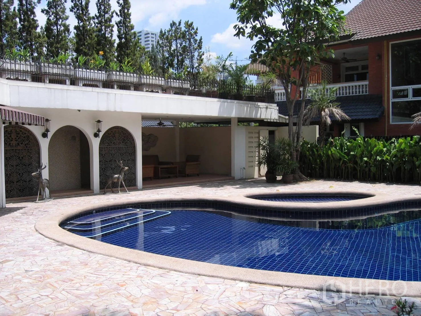 Detached House for rent in Watthana, Bangkok - Curved swimming pool with raised spa beside a shaded terrace with arched openings and greenery.