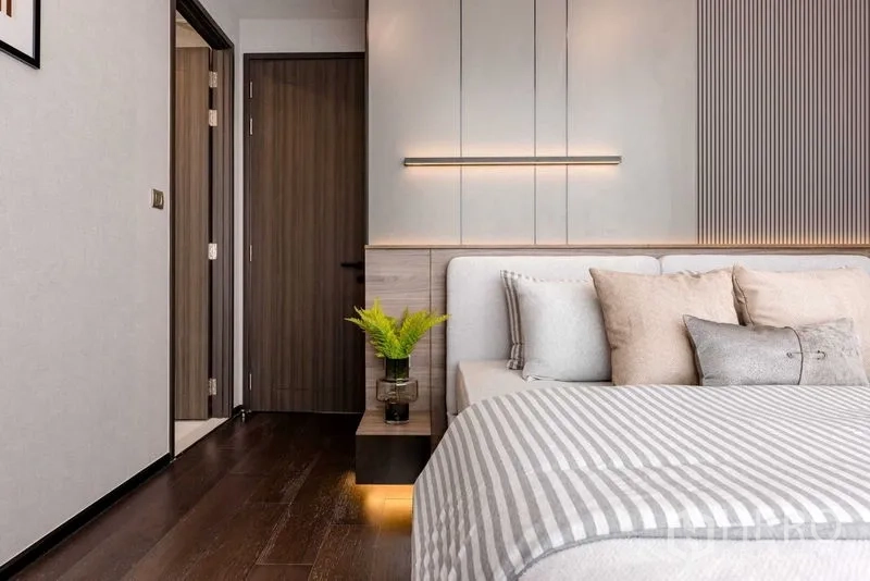 Condominium for rent in Watthana, Bangkok - Bedroom view toward doorway with bedside plant, wall lighting and wood flooring.