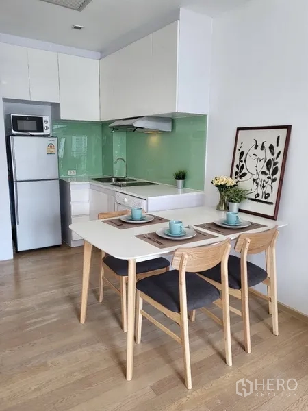 Condominium for rent in Bangkok - White kitchen with green glass backsplash, fridge, microwave and four-seat dining set.