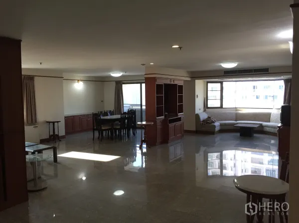 Condominium for rent in Watthana, Bangkok - Spacious open-plan living and dining area in a Watthana, Bangkok condominium with polished stone floors, built-in wood cabinetry, bay window and L-shaped sofa.