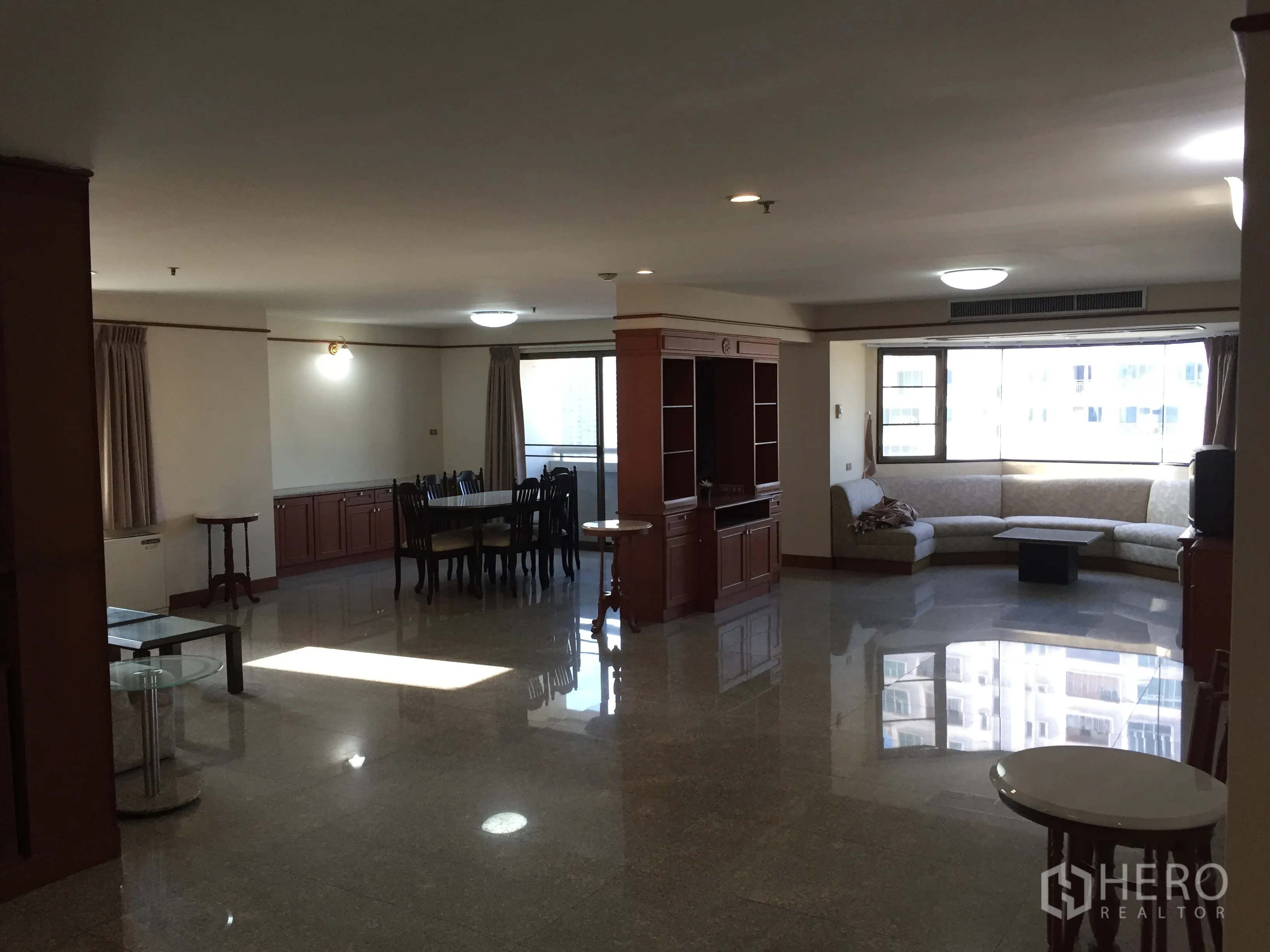 Condominium for rent in Watthana, Bangkok - Spacious open-plan living and dining area in a Watthana, Bangkok condominium with polished stone floors, built-in wood cabinetry, bay window and L-shaped sofa.