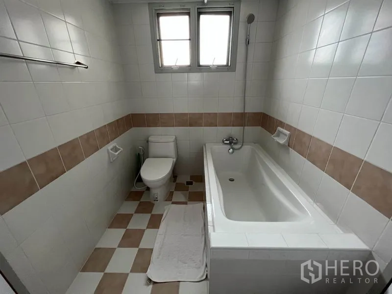 Condominium for rent or sale in Watthana, Bangkok - Bathroom with bathtub, handheld shower, white tiles with beige border and a window.