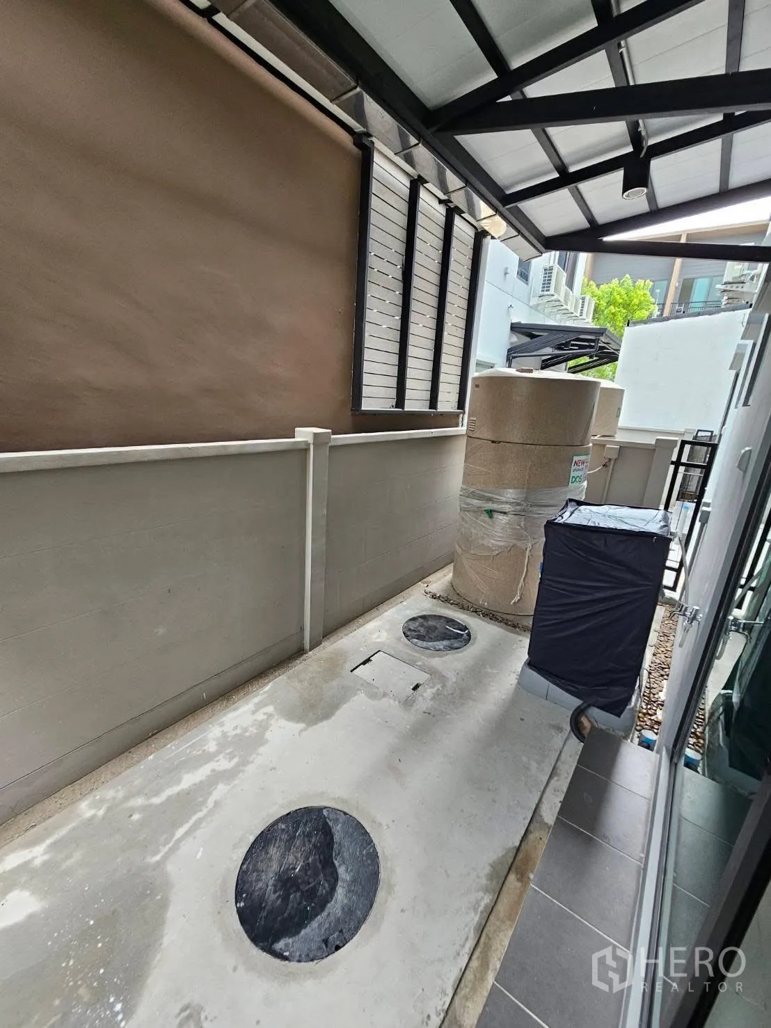Townhouse for rent in Saphan Sung, Bangkok - Covered side utility area with concrete floor, water tank, laundry space, and ventilation panels.
