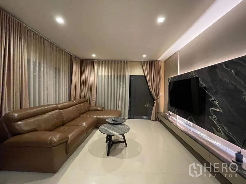 Detached House for rent or sale in Bang Phli, Samut Prakan - Modern living room with a brown leather sectional, marble TV feature wall and recessed lighting.