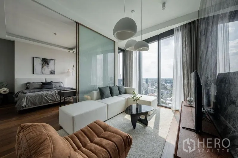 Condominium for rent in Khlong Toei, Bangkok - Stylish living space with white sectional sofa, pendant lights and panoramic windows.