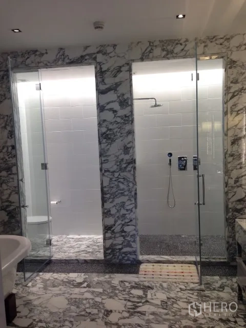 Condominium for rent or sale in Bang Rak, Bangkok - Elegant bathroom with twin glass-enclosed showers and marble walls and floors.
