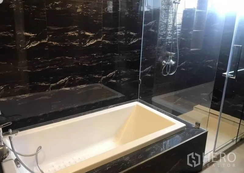 Condominium for rent in Khlong Toei, Bangkok - Deep soaking bathtub set against glossy black marble wall.