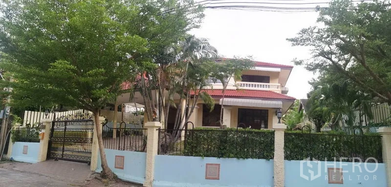 Detached House for sale - Street view of the detached house behind a wrought-iron fence and trees.