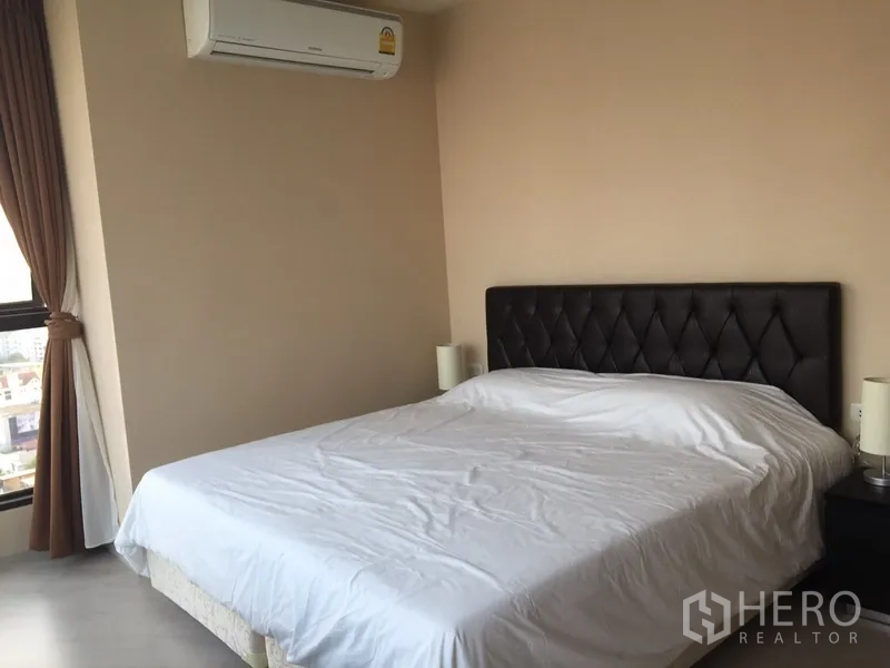 Condominium for rent in Khlong Toei, Bangkok - Second bedroom with upholstered headboard, large window and neutral décor for ample natural light.