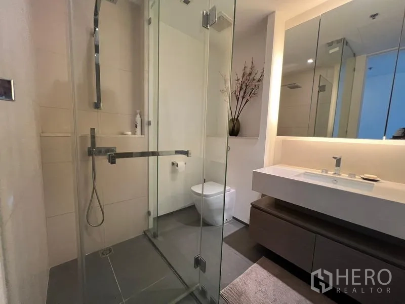 Condominium for sale in Khlong San, Bangkok - Bathroom with glass-enclosed shower, illuminated mirror, and floating vanity.