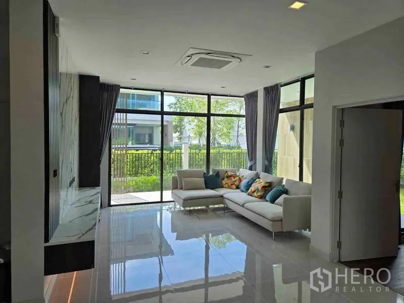 Detached House for rent in Bang Phli, Samut Prakan - Living room with L-shaped sofa, full-height windows and glossy tiled floors opening to the garden.
