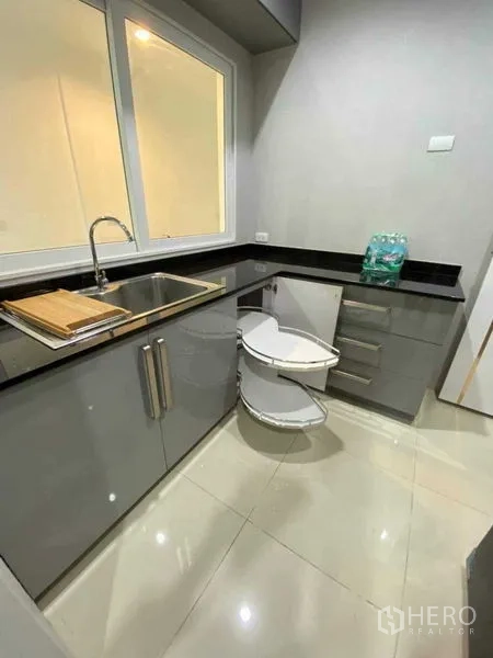 Detached House for rent in Bang Khen, Bangkok - L-shaped kitchen with black granite countertops, gray cabinets and corner carousel storage.