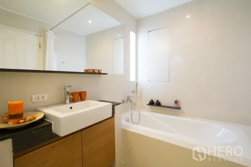 Apartment for rent in Watthana, Bangkok - Bathroom featuring a white bathtub, large mirror and square basin on a wood vanity.