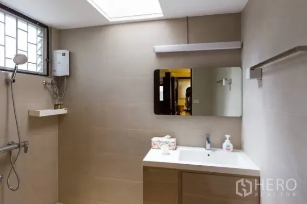 Detached House for rent in Watthana, Bangkok - Bright bathroom with beige tiles, vanity, skylight and walk‑in shower with water heater.
