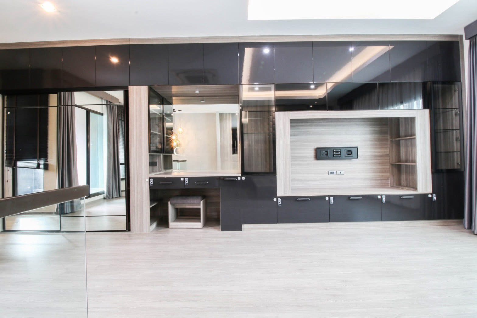 Townhouse for rent or sale in Lat Phrao, Bangkok - Modern room with full-height black gloss cabinets, mirrored panels, TV niche and light wood flooring.