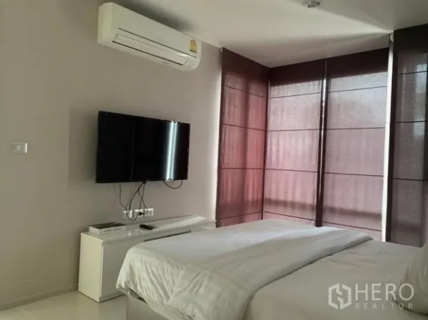公寓 出租在Khlong Toei, Bangkok - 卧室另一角，挂墙电视、空调与转角落地窗的深色窗帘。