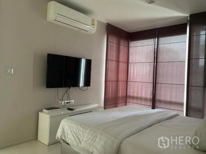 公寓 出租在Khlong Toei, Bangkok - 卧室另一角，挂墙电视、空调与转角落地窗的深色窗帘。