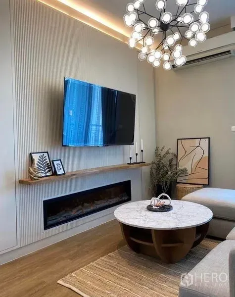 Condominium for rent in Ratchathewi, Bangkok - Stylish lounge with chandelier, mounted TV, electric fireplace, and marble coffee table on warm wood floors.