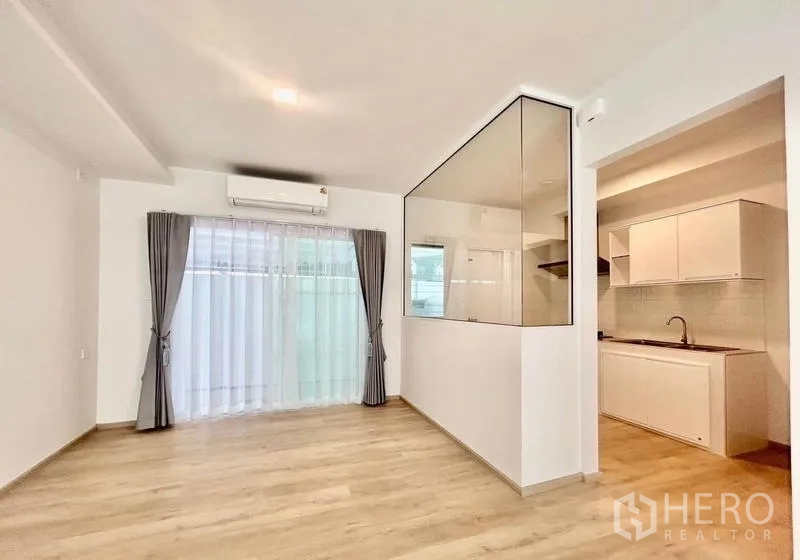 Townhouse for rent in Bang Phli, Samut Prakan - Bright living and dining area with wood floors, sheer curtains and a glass-partitioned kitchen.