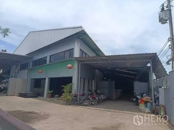 Warehouse for sale in Samut Sakhon - Two‑storey warehouse with metal roof, covered loading bay and parking area at the front entrance.